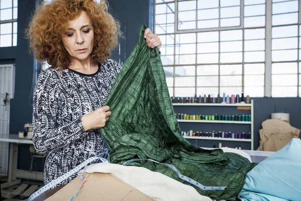 Mature female fashion designer measuring textiles on workshop table — Stock Photo