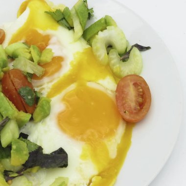 omlet ve salata dilimlenmiş avokado, domates, yeşil kereviz, taze kişniş ve fesleğen ile beyaz bir plaka üzerinde