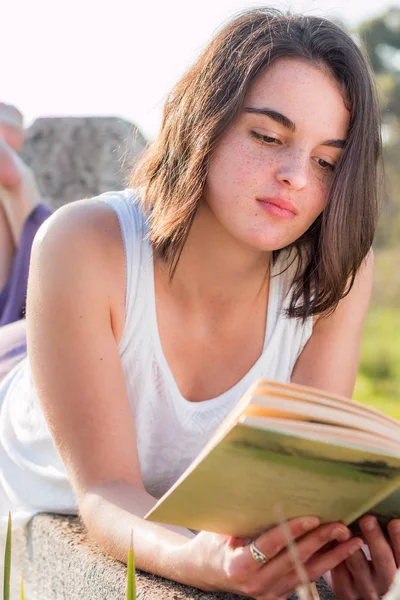 Menina que coloca ao ar livre livro de leitura — Fotografia de Stock