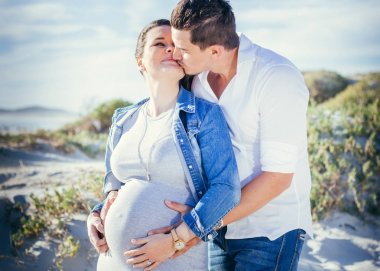 Etkileşim, ayakta açık havada öpüşme, mutlu hamile genç çift, kucaklayan rahat kıyafet ile plaj sahne.