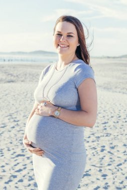 Açık havada beline tutarak ve gülümseyen, durmak mutlu hamile genç anne rahat kıyafet ile plaj sahnesi