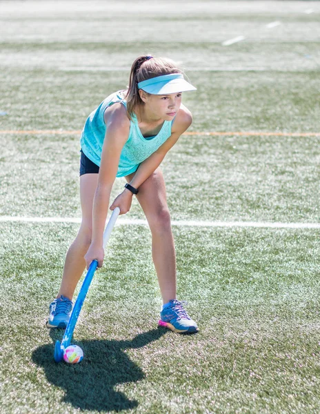 Sporty girl holding hockey stick standing ready to hit hockey ball on sports field.