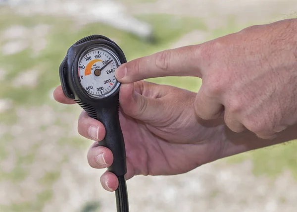 Hand holding a scuba diving equipment pressure gauge with finger pointing to the gauge face showing the pressure in the cylinder is at 210 bar.