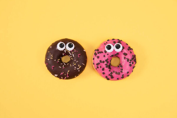 Красочные глазурованные пончики со смешными глазами на желтом фоне
.