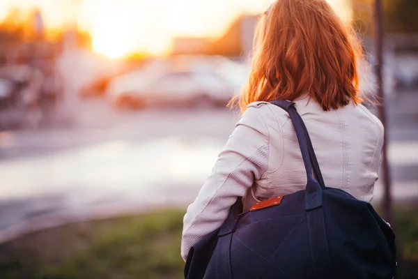 The girl with a leather bag against the background of cars.