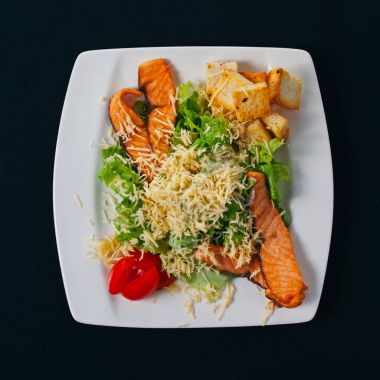 Ispanak ve mevsim sebzeleri salata beyaz plaka, siyah arka plan üzerinde ızgara somon