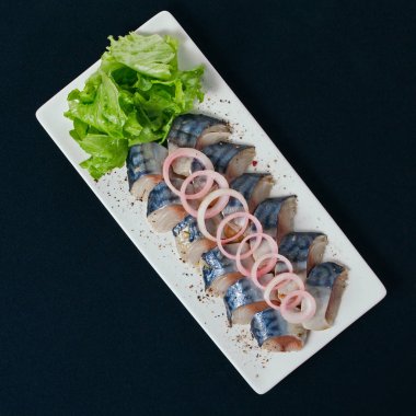 Otlar ve soğan dilimlenmiş ringa balığı. Beyaz tabak, siyah arka plan