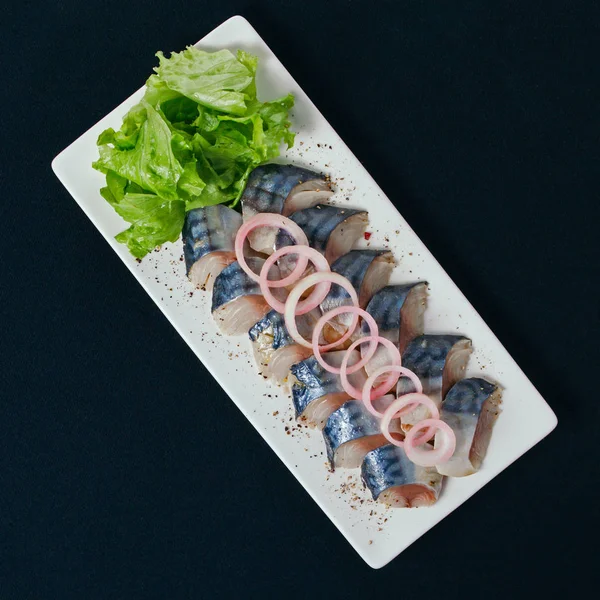 Otlar ve soğan dilimlenmiş ringa balığı. Beyaz tabak, siyah arka plan