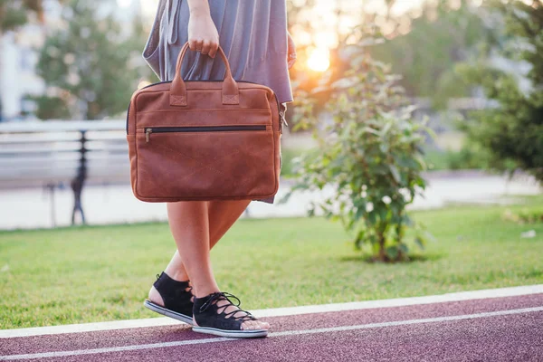 Herbst-Streetfashion-Look. junges brünettes Mädchen in grauem Strickkleid mit großer orangefarbener Ledertasche in der Hand im Park — Stockfoto