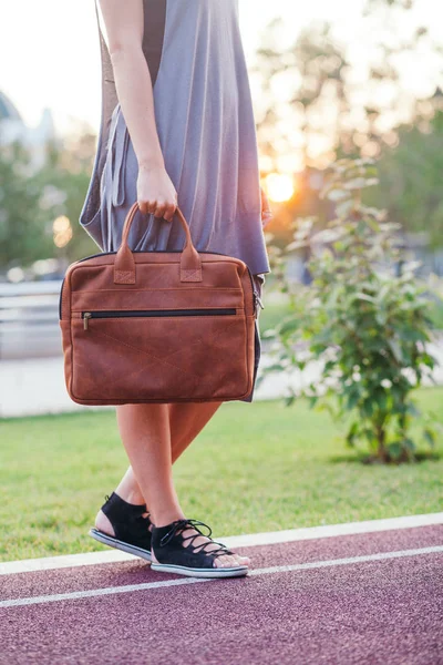 Herbst-Streetfashion-Look. junges brünettes Mädchen in grauem Strickkleid mit großer orangefarbener Ledertasche in der Hand im Park — Stockfoto