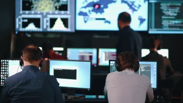 Team von Sicherheitspersonal beobachtet die Bildschirme in einem Systemkontrollzentrum. Dies könnte eine Wetterstation oder ein Flughafen-Kontrollraum sein. — Stockvideo