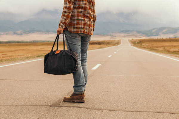 Человек с сумкой в руке, идущий по горной дороге
