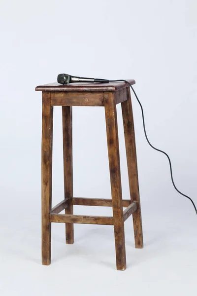 This is a photo of a microphone sitting on top of a wooden stool lite from above. Shot on a white background — Stock Photo, Image