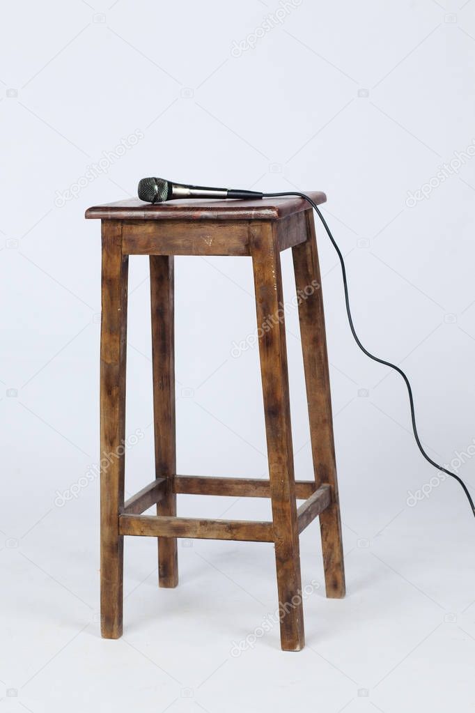 This is a photo of a microphone sitting on top of a wooden stool lite from above. Shot on a white background