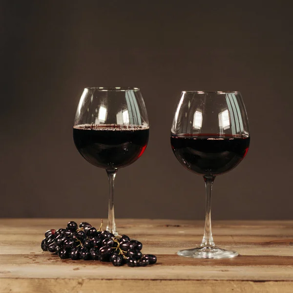 Two glasses of red wine and fresh grapes on dark wooden background — Stock Photo, Image