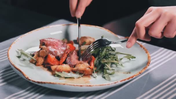 Закройте женские руки ножом и вилкой, разрезая мясо в тарелке на столе в ресторане — стоковое видео