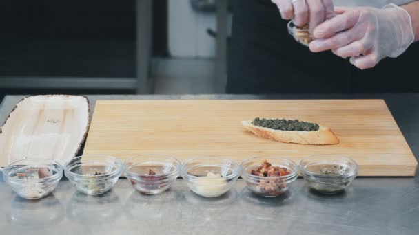 Chef-kok maakt bruschettes. Close up van smakelijke tapas op het houten bord in restaurants keuken. Zet het in een schotel — Stockvideo