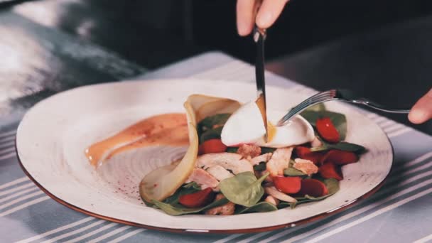 Las manos de las mujeres cortan huevo escalfado en ensalada con cuchillo y tenedor. Cúbrete. — Vídeos de Stock