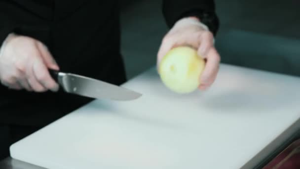 手拿洋葱。厨师切洋葱在白色的切割板特写。在餐厅厨房做饭。手把刀子放在黑板上 — 图库视频影像