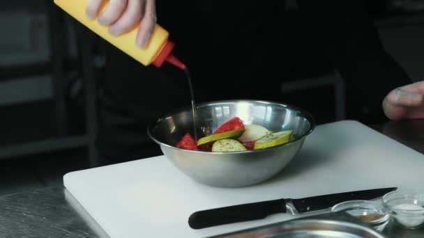 Chef kok stromende olie en saus uit de fles op groenten in metalen plaat op een witte snijplank — Stockvideo