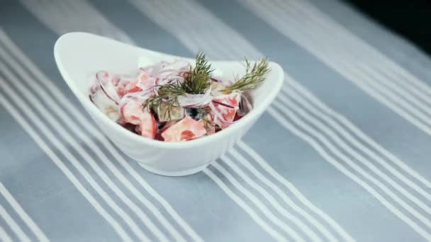 Una mano femenina gira un plato blanco con una ensalada sobre la mesa. En el fondo un mantel azul en tiras — Vídeos de Stock