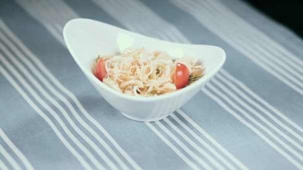 Una mano femenina gira un plato blanco con una ensalada sobre la mesa. En el fondo un mantel azul en tiras — Vídeos de Stock