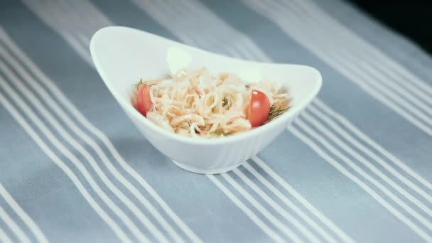 Uma mão feminina vira um prato branco com uma salada na mesa. No fundo uma toalha de mesa azul em umas tiras — Vídeo de Stock