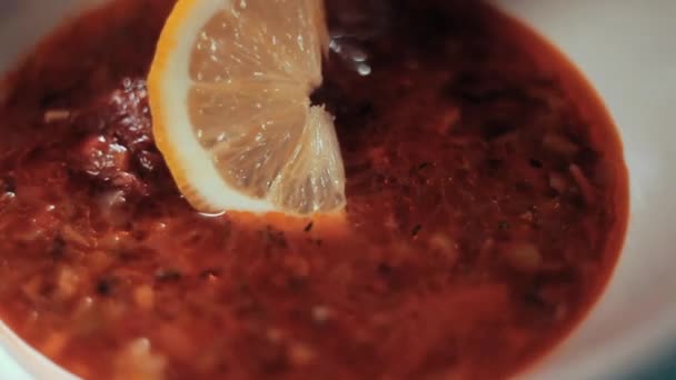 Clouse van voedsel. De chef-kok brengt een schijfje citroen in de soep en de hagelslag met kruiden. Traditionele Russische soep Solyanka met vlees, augurken, schijfjes worst en olijven. — Stockvideo