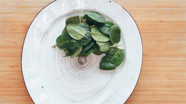 Bovenaanzicht. Clouse van voedsel. De chef-kok legt de salade op een witte plaat. Salade van spinazie, kip, eieren, gepocheerd onder de saus. Een plaat op een houten tafel. — Stockvideo