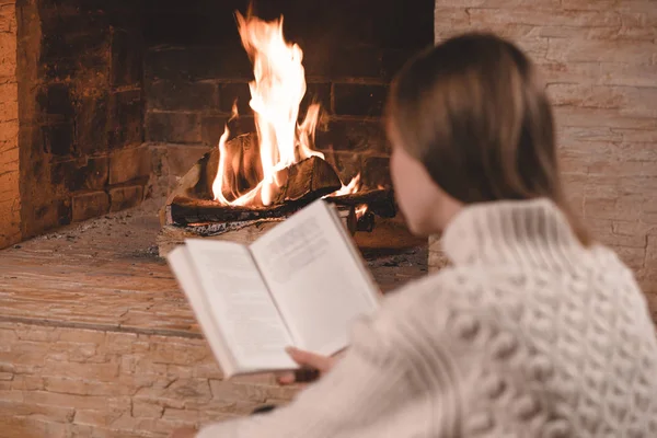 Söt ung flicka läser bok vid öppen spis hemma — Stockfoto