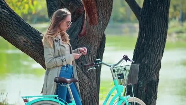 Jonge vrouw in jas met vintage fiets in de buurt van vijver — Stockvideo