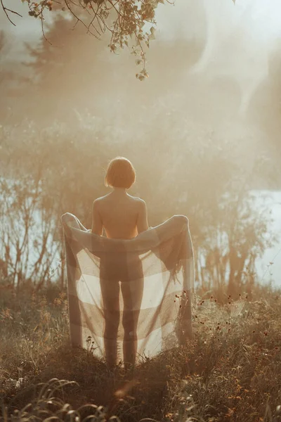Молодая женщина у озера на рассвете в одеяле — стоковое фото