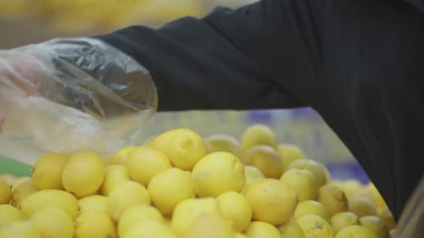 Der Mann legt statt Handschuhen eine Tasche auf die Hand und wählt im Supermarkt eine Zitrone — Stockvideo