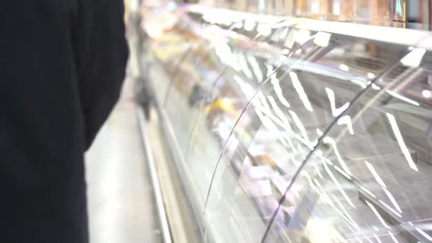 Un hombre con guantes protectores y una máscara pasa junto a los estantes vacíos del supermercado . — Vídeos de Stock