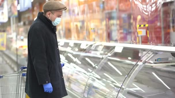 Ein Mann mit Schutzhandschuhen und Maske vor leeren Regalen in einem Supermarkt. — Stockvideo