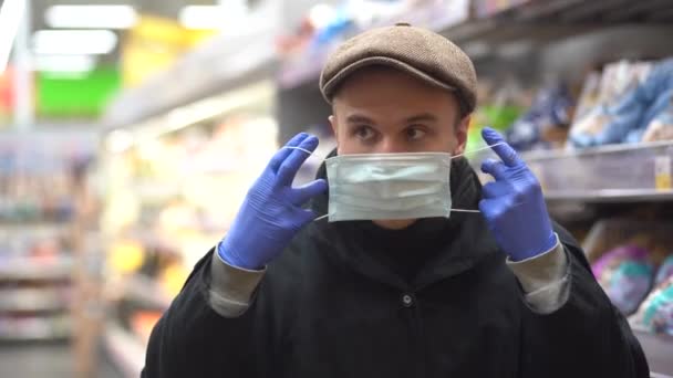 Een jonge man met een pet zet een medisch masker op om te beschermen tegen de epidemie, een close-up portret op de markt. Bescherming tegen de coronaviruspandemie — Stockvideo