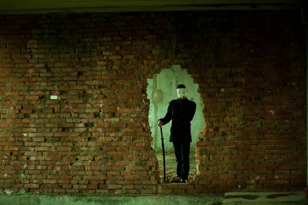 L'homme en noir avec une épée de samouraï katana dans un bâtiment abandonné à travers le mur — Photo