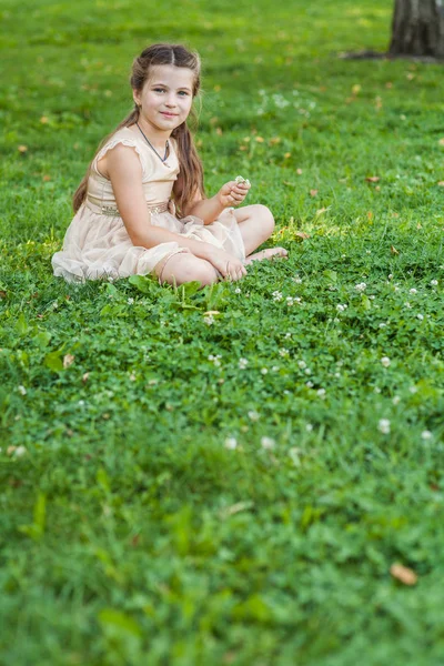Fille en robe dorée assise sur la pelouse avec un bouquet de fleurs — Photo