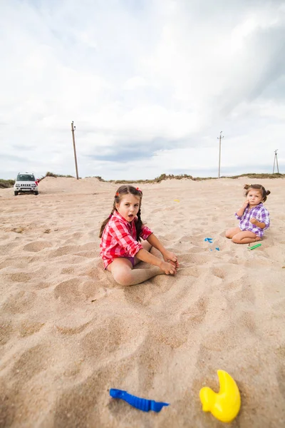 Mladá dívka v košili si hraje na písčité pláži s lopatou — Stock fotografie