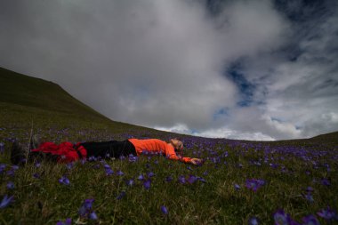 kadın turist bir arka planını çiçekler arasında dağlar bir tepe üstünde dinlenme yalan
