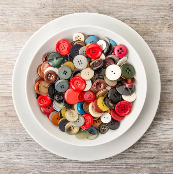 A lot of buttons in dish in wooden background — Stock Photo, Image