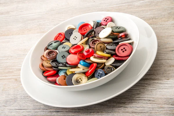 A lot of buttons in dish in wooden background — Stock Photo, Image