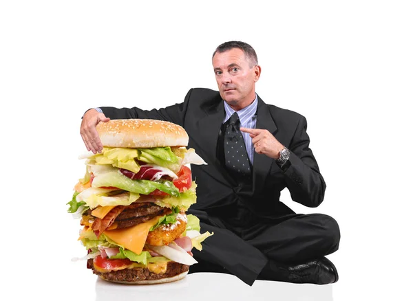 Hombre de negocios sentado cerca de un gran sándwich en fondo blanco — Foto de Stock