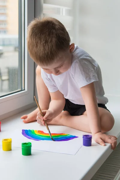 Boy sitting on the windowsill draws the rainbow for the chasetherainbow project