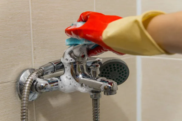 Hand in rubber glove cleans dirty calcified shower mixer tap, close up photo
