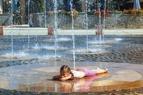 Girl on a sunny warm day playing outside in a water fountain. Girl happily in shallow clean water on of city fountain on warm bright summer day.