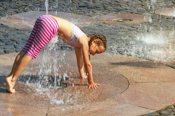 Girl on a sunny warm day playing outside in a water fountain. Girl happily in shallow clean water on of city fountain on warm bright summer day.