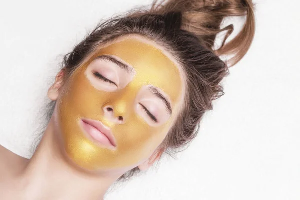Mooi meisje met een cosmetische masker op het gezicht van gouden kleur. Close-up. Vrije ruimte. Vrouw gouden masker. Mooi model gouden gezichtshuid cosmetische verwijderen. Beauty huidverzorging . — Stockfoto