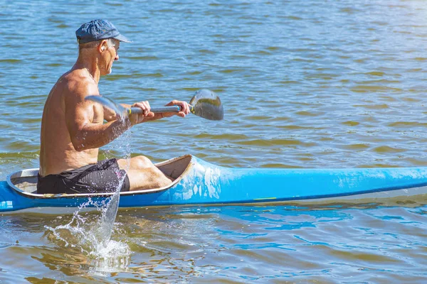 Homme pagayant un kayak bleu et jaune sur la rivière près de la rive. Concept de kayak.Un homme nage dans un canot sur la rivière. Un homme dans un bateau par une belle journée d'été. Bateau bleu et jaune . — Photo