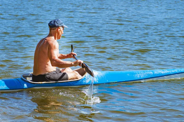 Man paddlar en blå och gul kajak på ån nära stranden. Kajakkonceptet. En man simmar i en kanot på ån. En man i en båt en solig sommardag. Blå och gul båt. — Stockfoto